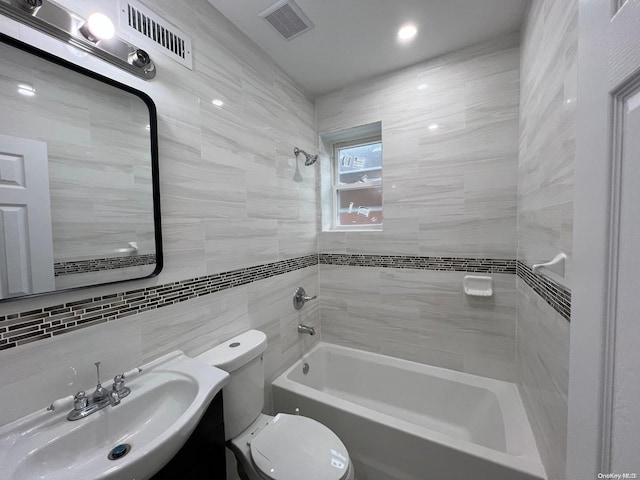 full bathroom with sink, decorative backsplash, tiled shower / bath combo, toilet, and tile walls