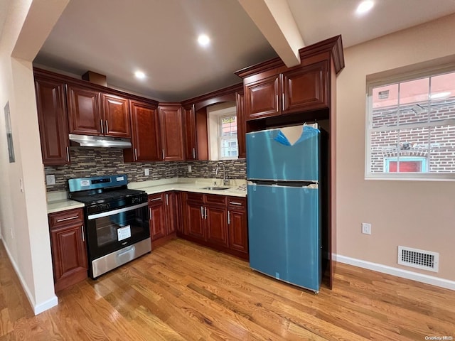 kitchen with backsplash, sink, light hardwood / wood-style floors, beam ceiling, and stainless steel appliances