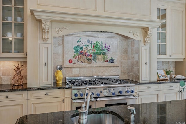 kitchen featuring high end stainless steel range, decorative backsplash, dark stone counters, and cream cabinets