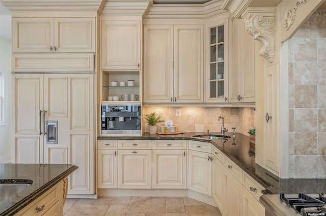 kitchen featuring decorative backsplash, sink, light tile patterned floors, dark stone countertops, and cream cabinetry