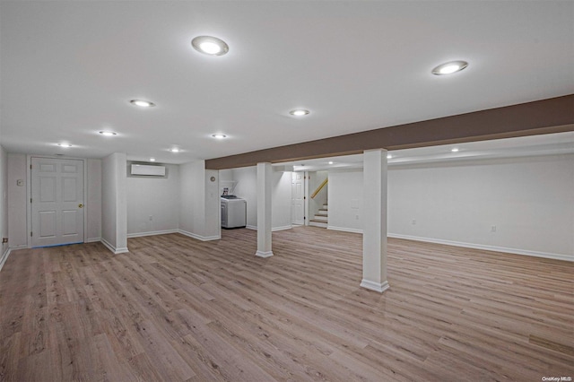 basement featuring light hardwood / wood-style floors, an AC wall unit, and washer / clothes dryer