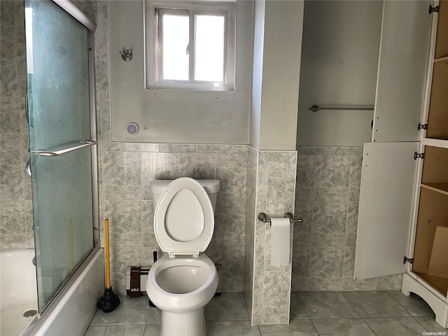 bathroom featuring toilet, enclosed tub / shower combo, and tile walls