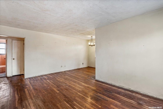 spare room with a textured ceiling, a chandelier, and dark hardwood / wood-style floors