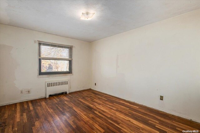 empty room featuring radiator, dark wood-type flooring, and a textured ceiling