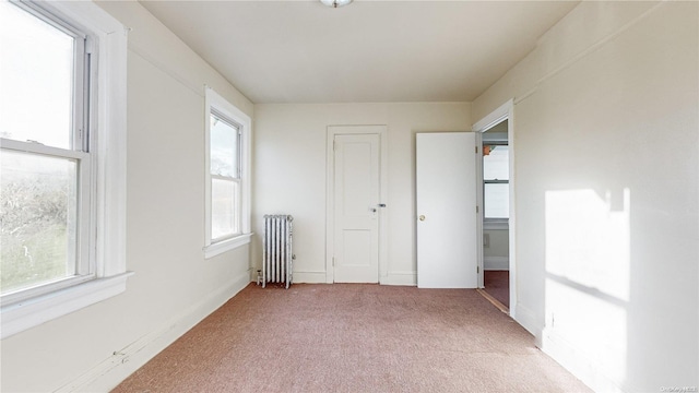 unfurnished bedroom featuring radiator heating unit, light carpet, and multiple windows