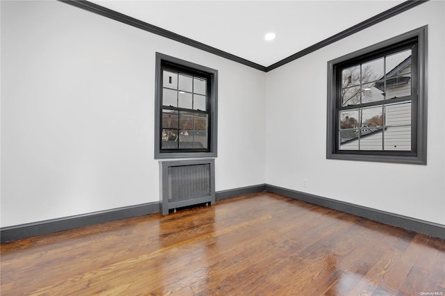 empty room with hardwood / wood-style flooring, radiator heating unit, crown molding, and a wealth of natural light