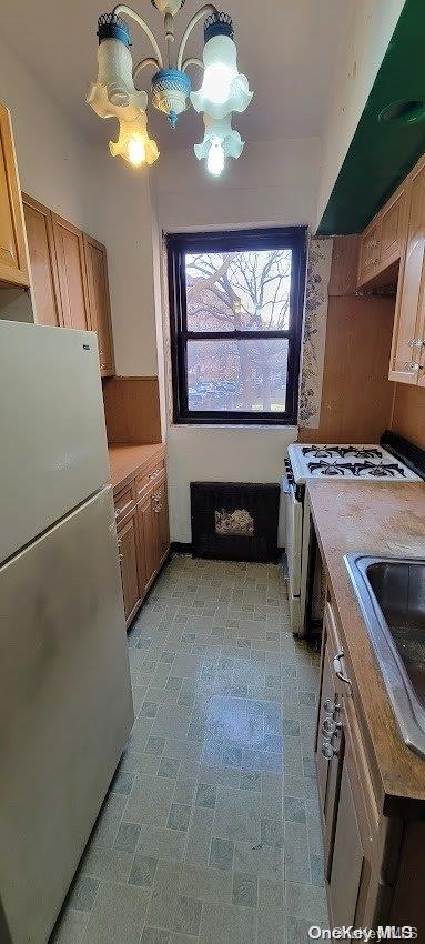 kitchen with stainless steel refrigerator, sink, white range, a notable chandelier, and light brown cabinetry