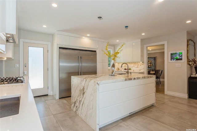 kitchen with tasteful backsplash, stainless steel appliances, a center island with sink, white cabinetry, and light tile patterned flooring