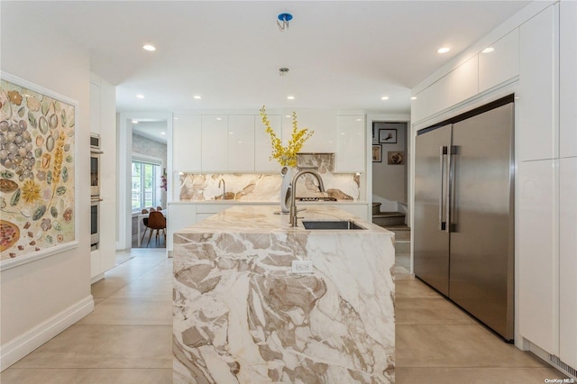 kitchen with backsplash, stainless steel appliances, a kitchen island with sink, sink, and white cabinetry