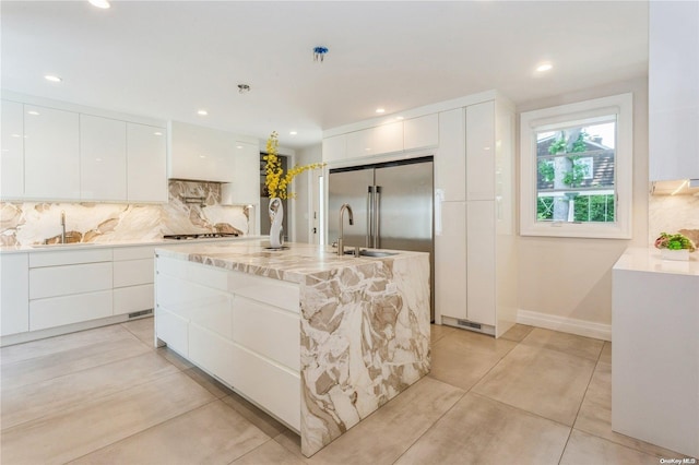 kitchen with white cabinets, sink, backsplash, and an island with sink