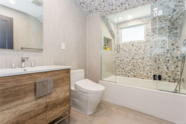 full bathroom with vanity, tile patterned floors, bath / shower combo with glass door, toilet, and tile walls