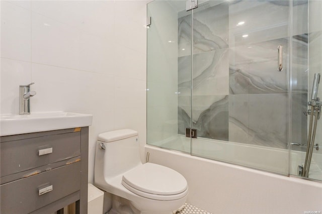 full bathroom featuring vanity, bath / shower combo with glass door, tile walls, and toilet