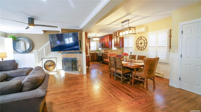 dining room featuring ornamental molding, ceiling fan, a baseboard radiator, hardwood / wood-style flooring, and a stone fireplace