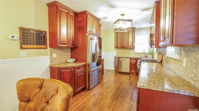 kitchen with light stone countertops, sink, hanging light fixtures, stainless steel appliances, and light wood-type flooring