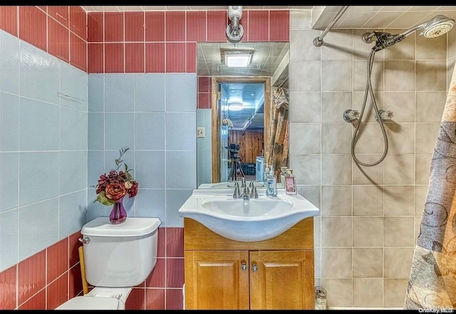 bathroom featuring vanity, toilet, tile walls, and a tile shower