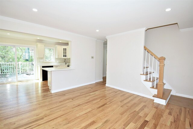 unfurnished living room with light wood-type flooring, a sink, ornamental molding, stairway, and baseboards