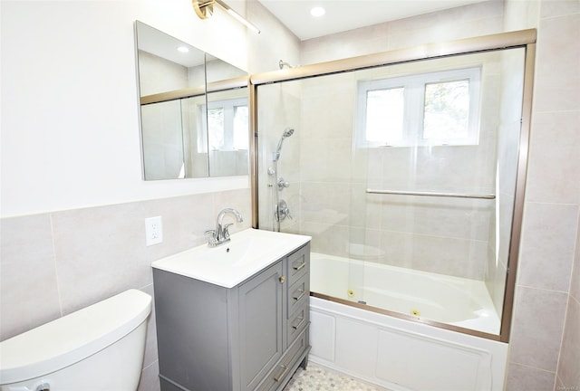 bathroom with tile walls, plenty of natural light, toilet, a combined bath / shower with jetted tub, and vanity