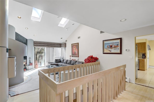 interior space featuring light wood-type flooring, a skylight, high vaulted ceiling, and a baseboard heating unit