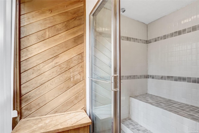 bathroom featuring a shower with door and wooden walls