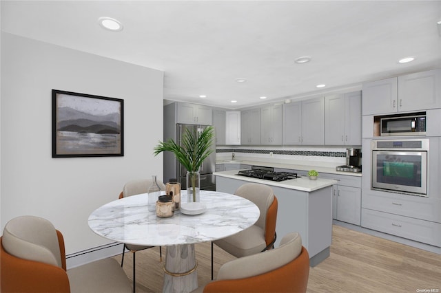 kitchen with a baseboard heating unit, appliances with stainless steel finishes, decorative backsplash, a kitchen island, and light wood-type flooring