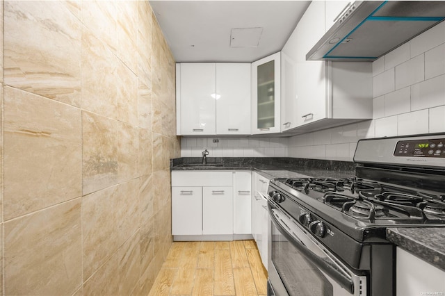 kitchen featuring dark stone counters, stainless steel gas range, white cabinets, light hardwood / wood-style floors, and range hood