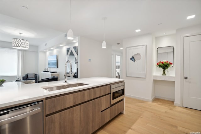 kitchen with pendant lighting, sink, stainless steel appliances, and light hardwood / wood-style flooring