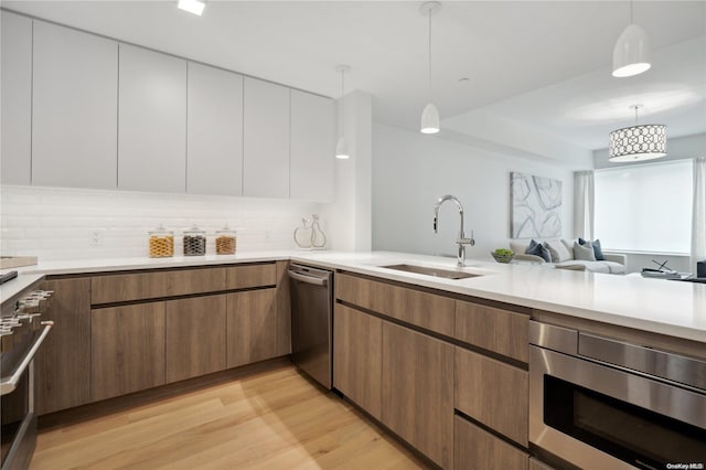 kitchen with white cabinetry, sink, light hardwood / wood-style floors, pendant lighting, and appliances with stainless steel finishes