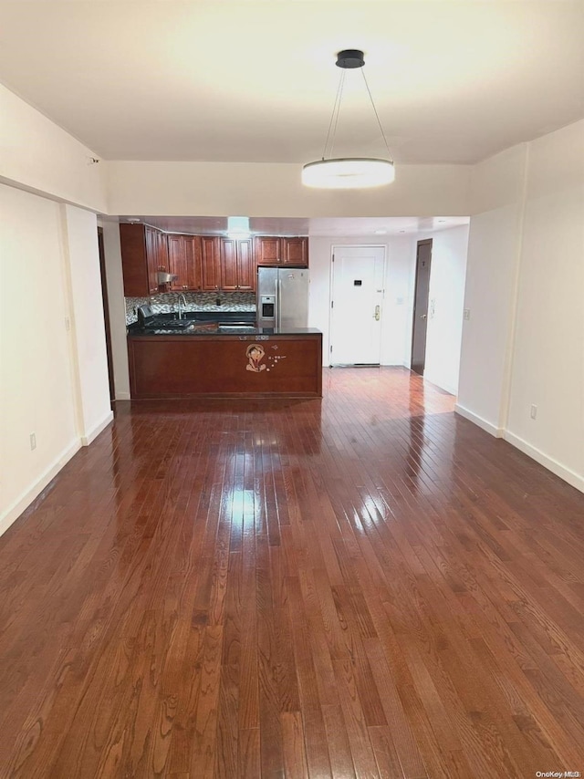 kitchen with kitchen peninsula, stainless steel fridge, tasteful backsplash, dark hardwood / wood-style floors, and hanging light fixtures