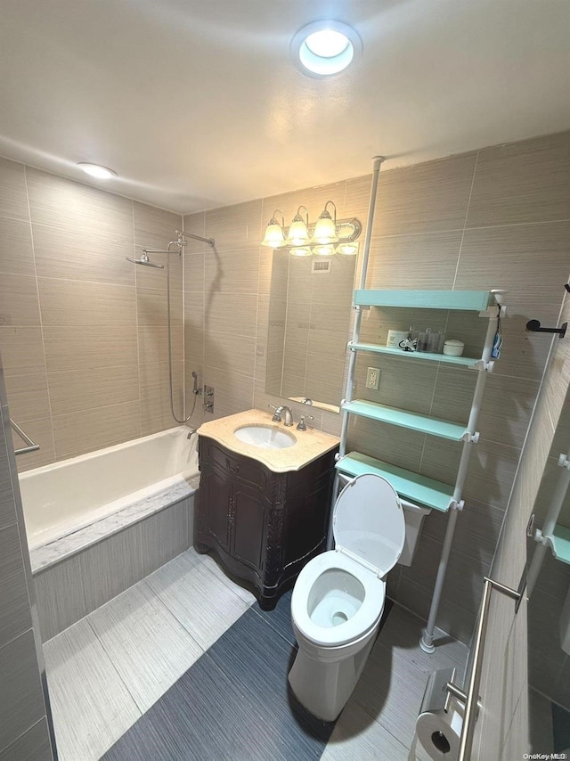 full bathroom with vanity, tiled shower / bath, tile patterned flooring, toilet, and tile walls