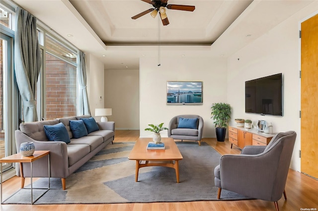 living room with a raised ceiling, ceiling fan, and light hardwood / wood-style flooring