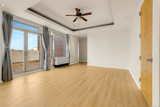 spare room with ceiling fan, light hardwood / wood-style floors, a raised ceiling, and french doors