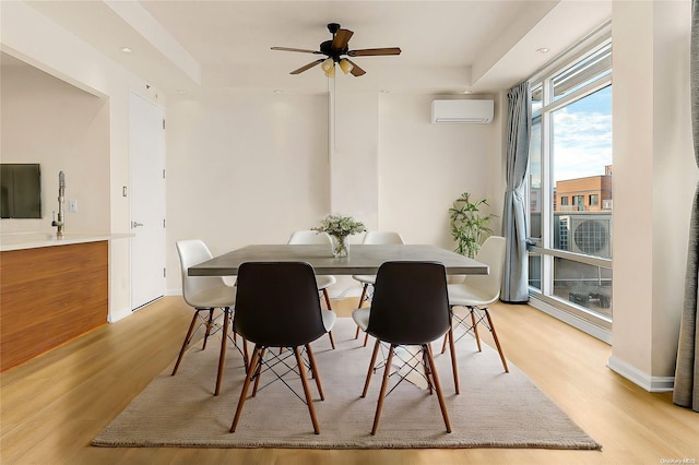 dining area featuring a wall mounted air conditioner, ceiling fan, light wood-type flooring, and a tray ceiling