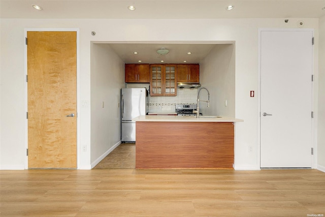 kitchen with stainless steel refrigerator, decorative backsplash, sink, and light wood-type flooring