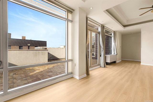 empty room with ceiling fan, a raised ceiling, and light wood-type flooring