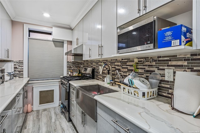 kitchen with light stone countertops, stainless steel appliances, light hardwood / wood-style flooring, backsplash, and crown molding