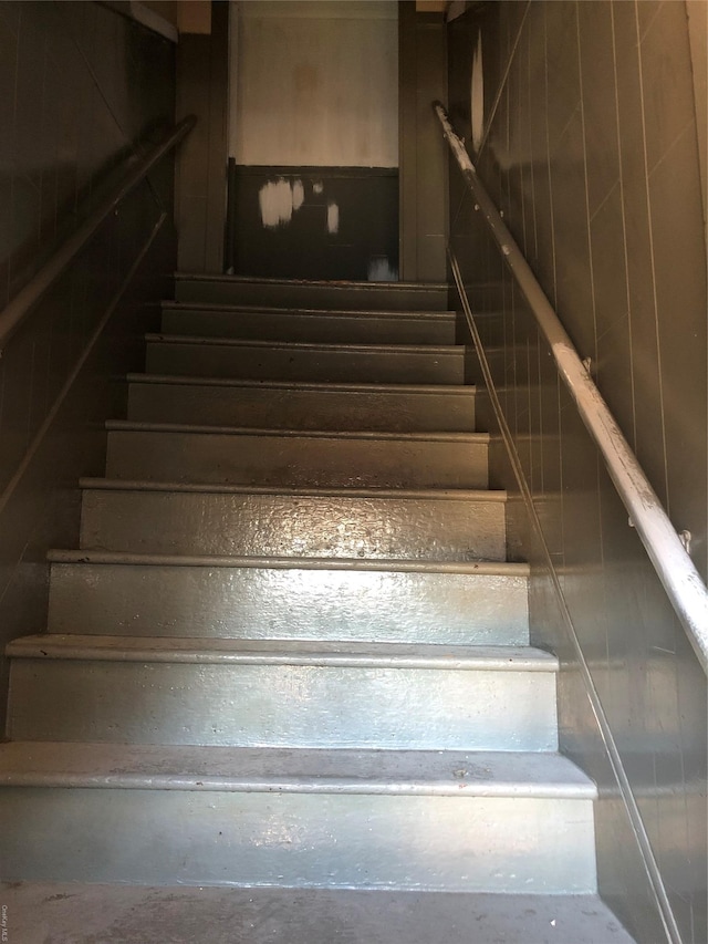 stairway featuring concrete flooring and wood walls