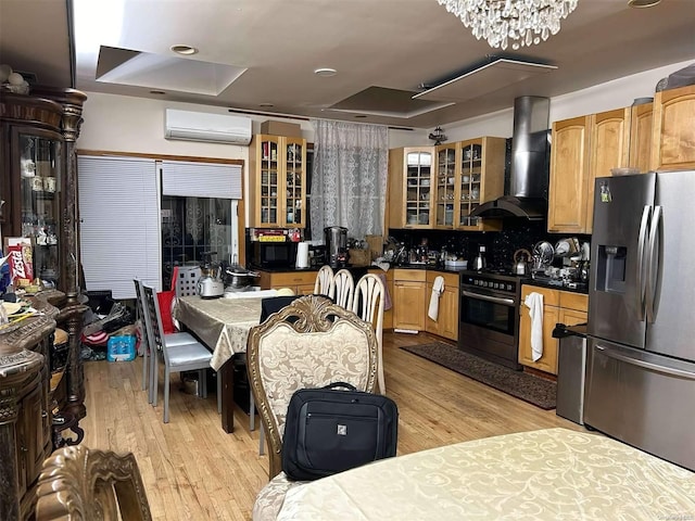 kitchen with a wall mounted air conditioner, light wood-type flooring, stainless steel appliances, exhaust hood, and a chandelier