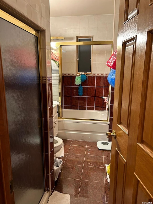 bathroom featuring tile patterned flooring, bath / shower combo with glass door, and tile walls