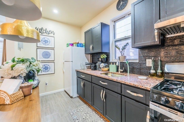 kitchen with stainless steel gas range oven, backsplash, ventilation hood, white refrigerator, and sink