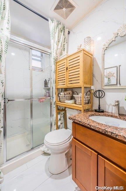 bathroom featuring vanity, tile patterned flooring, toilet, walk in shower, and tile walls