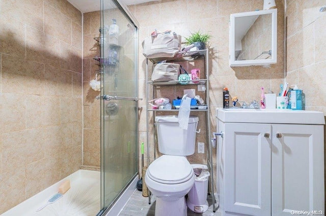 bathroom with vanity, toilet, a shower with door, and tile walls