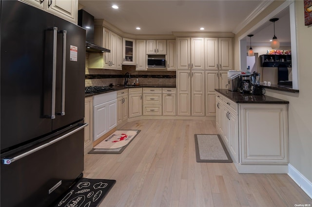 kitchen with light wood-type flooring, stainless steel appliances, wall chimney range hood, sink, and pendant lighting