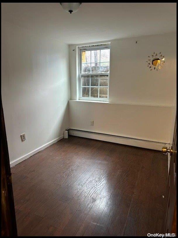 unfurnished room featuring dark wood-type flooring and a baseboard heating unit