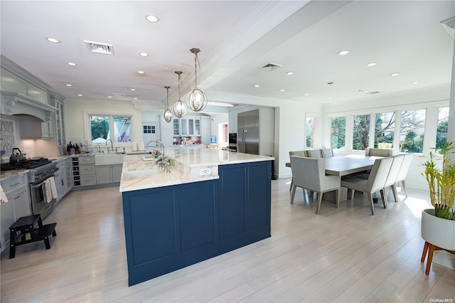 kitchen with light stone countertops, a large island with sink, decorative light fixtures, high end stainless steel range, and gray cabinets