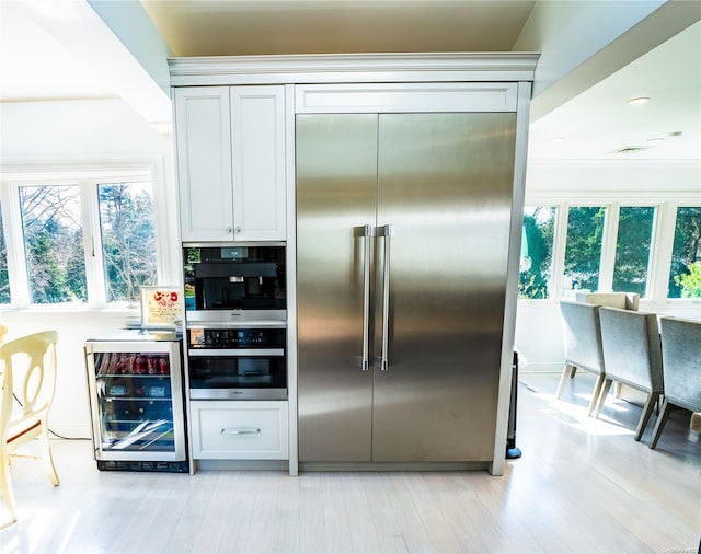 kitchen with wine cooler, white cabinetry, appliances with stainless steel finishes, and light hardwood / wood-style flooring