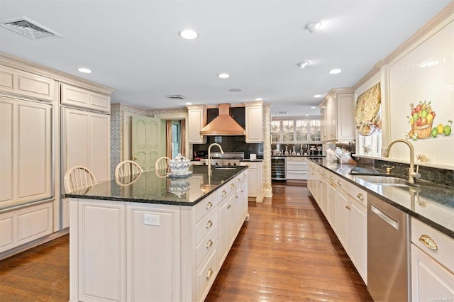 kitchen featuring dishwasher, sink, dark stone counters, a center island with sink, and hardwood / wood-style flooring