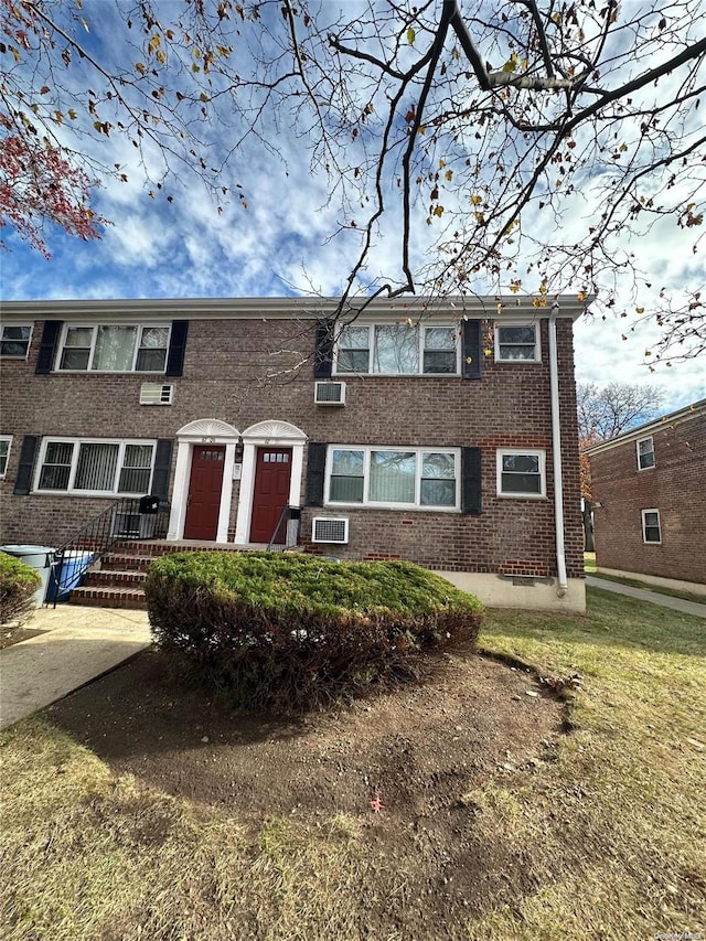 townhome / multi-family property featuring a wall mounted air conditioner and a front lawn