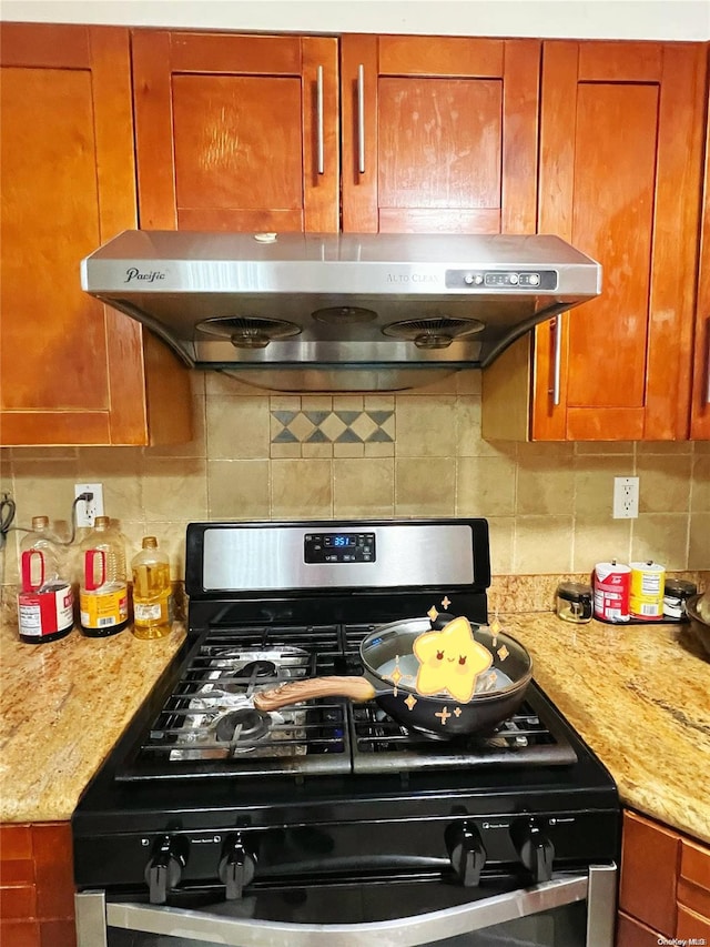 kitchen with decorative backsplash, light stone countertops, range hood, and stainless steel range with gas stovetop