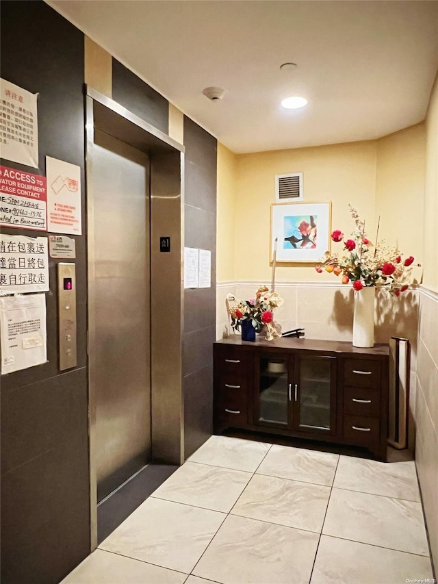 interior space with dark brown cabinets, elevator, tile walls, and light tile patterned flooring