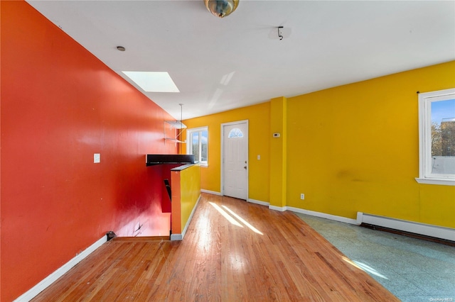 entrance foyer with baseboard heating, a skylight, plenty of natural light, and wood-type flooring